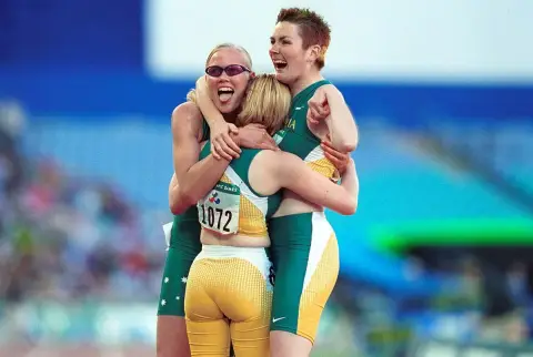 Three Australian athletes in green and gold hug and cheer on the track at the 2000 Sydney Paralympic Games.
