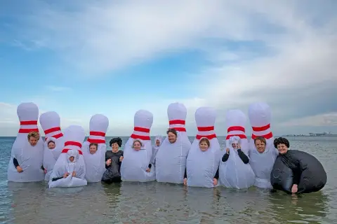 A group in inflatable bowling-pin costumes stand together in the shallows at the Polar Plunge for Special Olympics in South Melbourne.