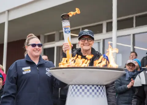 Two women in jackets smile beside a flaming torch cauldron at the Polar Plunge for Special Olympics in South Melbourne.