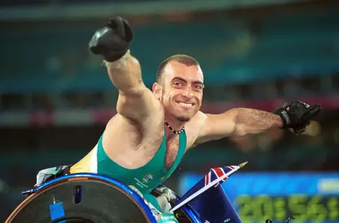 Wheelchair racer Paul Nunnari stretches an arm out and grins in his racing chair in the stadium at the 2000 Sydney Paralympic Games.