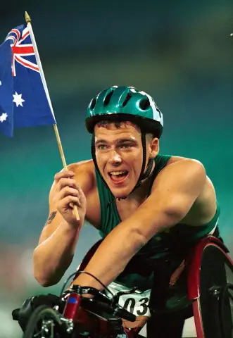 Wheelchair racer Kurt Fearnley laughs in his helmet and holds an Australian flag after a race at the 2000 Sydney Paralympic Games.