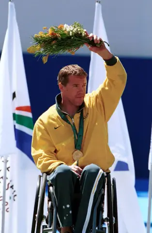 Wheelchair racer Greg Smith waves a bouquet from the gold medal podium at the 2000 Sydney Paralympic Games.