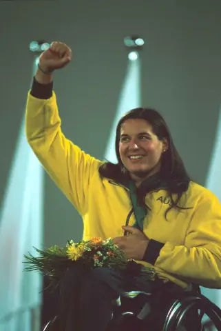 Wheelchair racer Louise Sauvage smiles with her fist raised and a bouquet in her lap on the medal podium at the 2000 Sydney Paralympic Games.