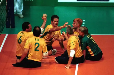 The Australian sitting volleyball team, in gold jerseys, cheer in a huddle on the court at the 2000 Sydney Paralympic Games.