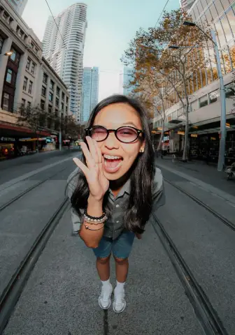 A young woman in glasses cups her hands round her mouth and laughs on a Sydney city street, shot from above with a wide lens.