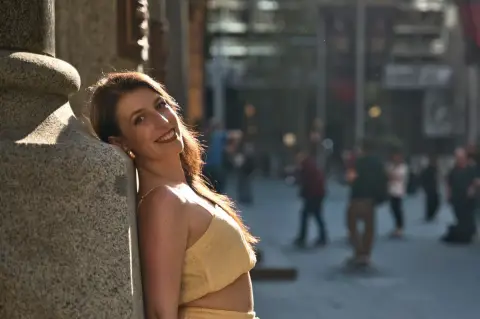A woman in a yellow top leans against a stone pillar and smiles warmly on a Sydney city street.