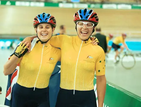 Tandem cyclists Tania Modra and Sarnya Parker, in helmets and gold Australian jerseys, hug and laugh at the velodrome at the 2000 Sydney Paralympic Games.