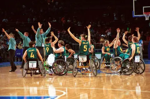The Australian women's wheelchair basketball team raise their arms together in celebration on court at the 2000 Sydney Paralympic Games.
