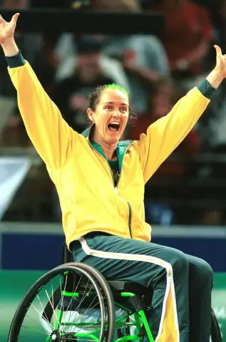 A wheelchair basketball player in an Australian tracksuit throws both arms in the air with a huge smile at the 2000 Sydney Paralympic Games.