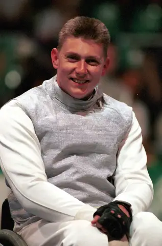 Wheelchair fencer Michael Alston smiles to camera in his white fencing jacket at the 2000 Sydney Paralympic Games.